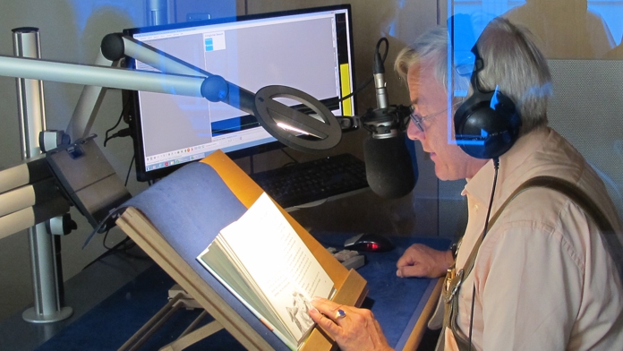 Der Sprecher, Anfang 60, sitzt im Tonstudio. Er blickt auf das Buch, das aufgeschlagen vor ihm liegt, und spricht den Text in das Mikrofon.